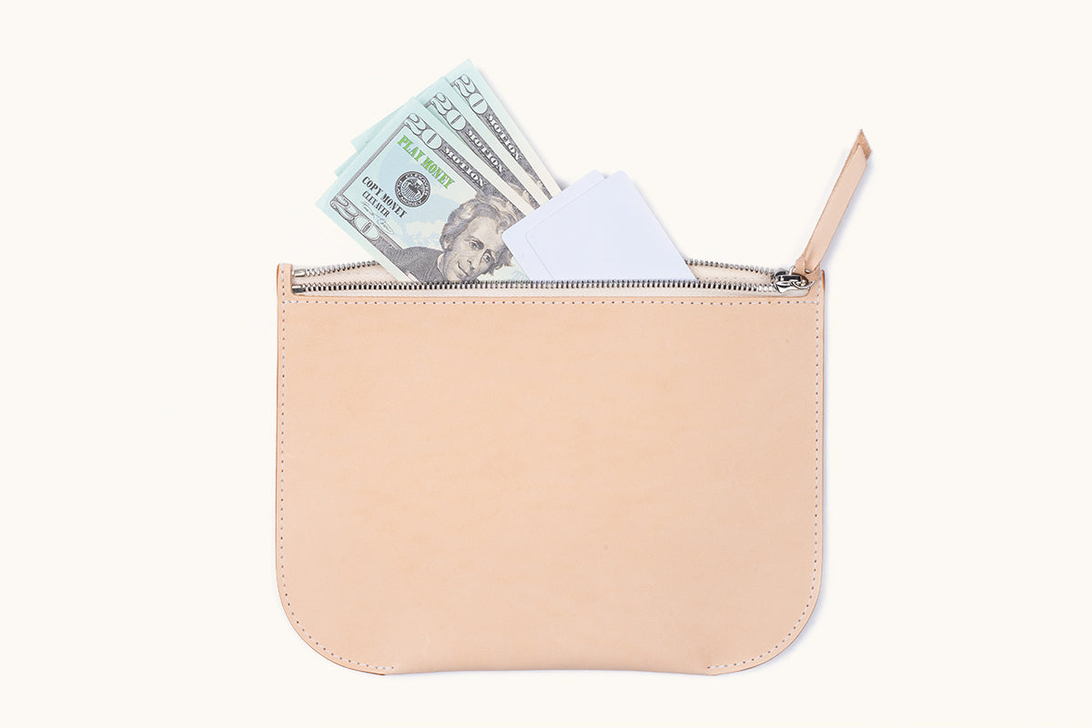 Light tan leather Universal Zip Pouch with a silver zipper, containing play money and white cards.