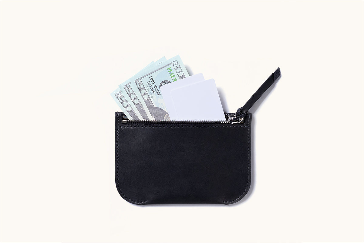Black leather universal zip pouch displayed from above, partially open, containing light blue play money and white cards.