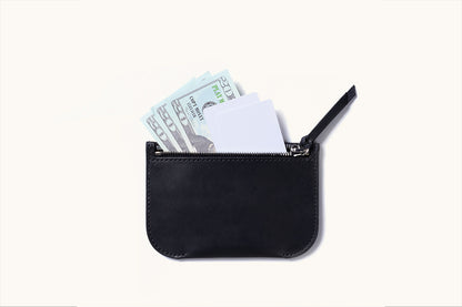 Black leather universal zip pouch displayed from above, partially open, containing light blue play money and white cards.