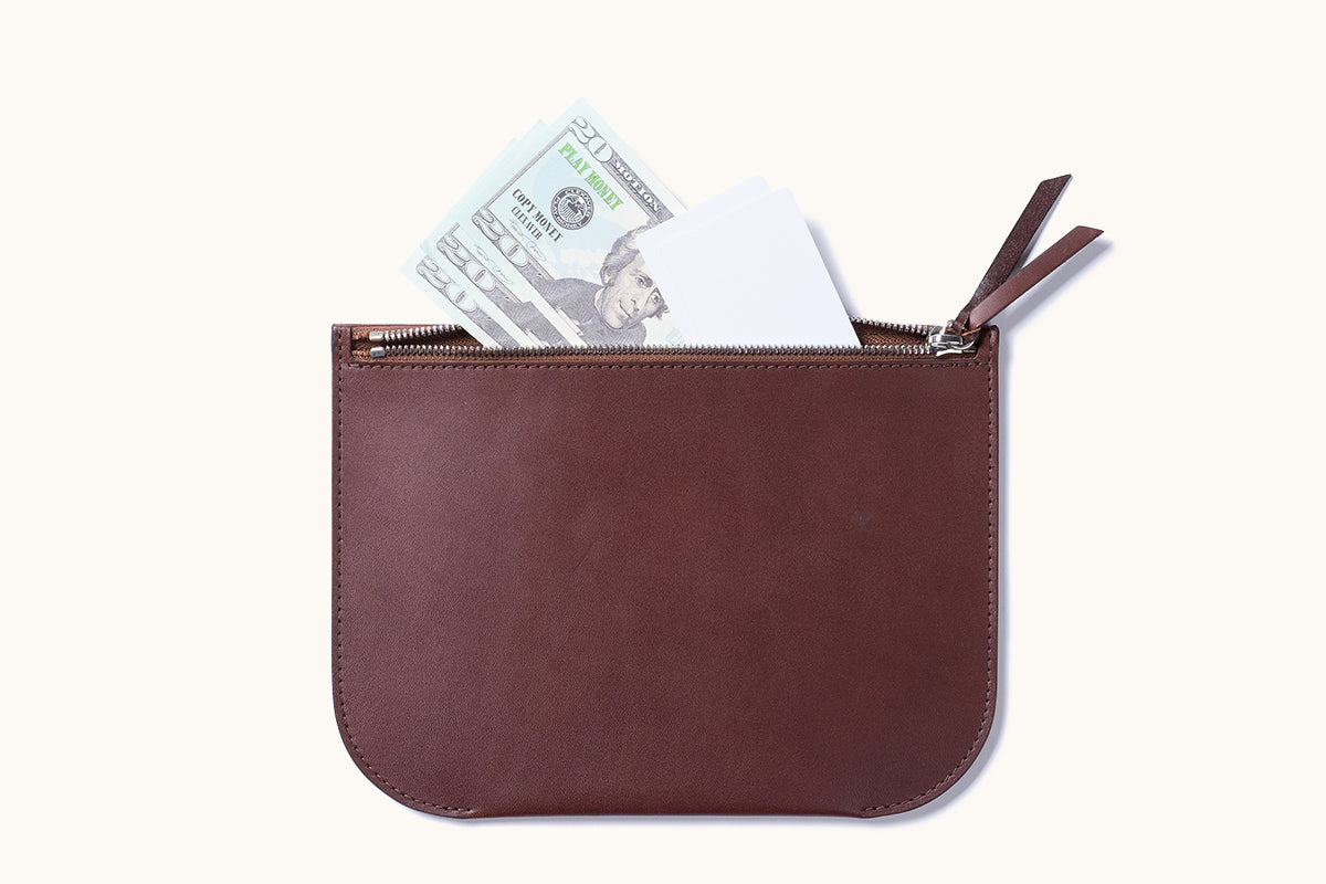 Open brown leather zip pouch with a metal zipper and leather pull tabs, holding play money and white cards.