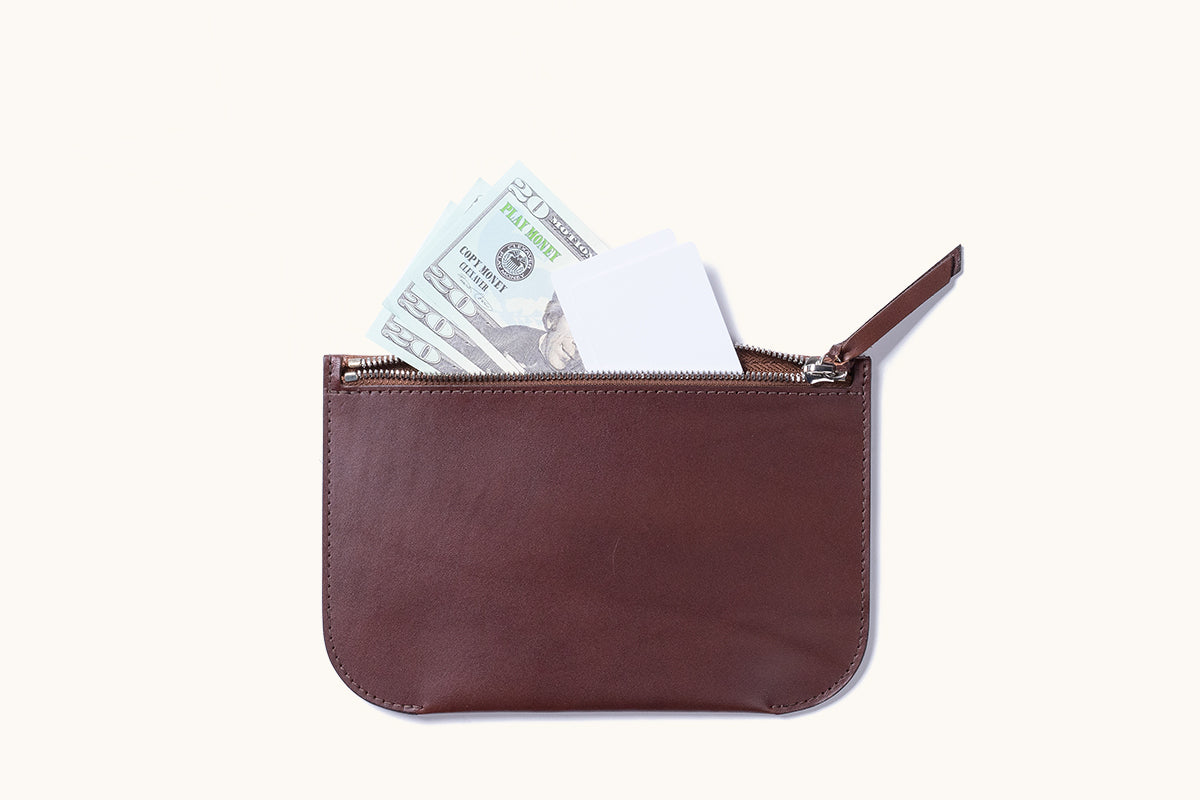 Brown leather Universal Zip Pouch open with play money and white cards peeking out.