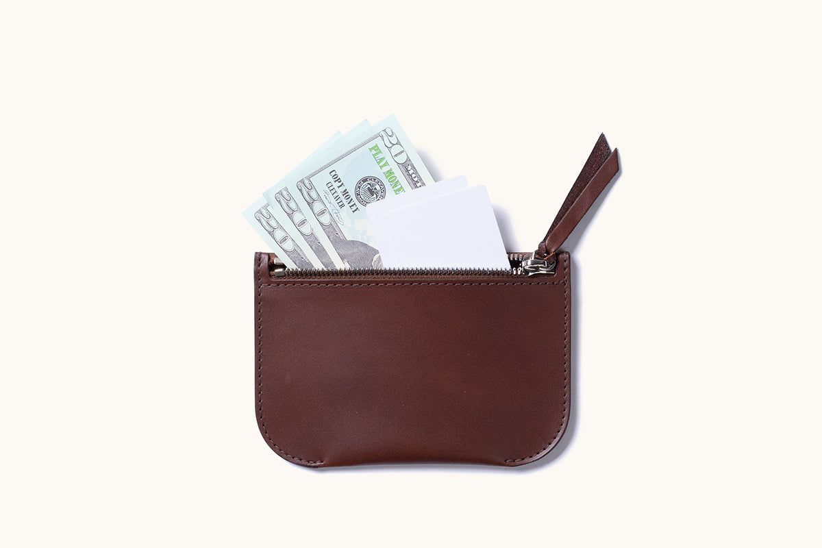 Dark brown leather Universal Zip Pouch with an open zipper revealing white cards and play money.