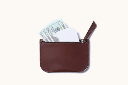 Dark brown leather Universal Zip Pouch with an open zipper revealing white cards and play money.