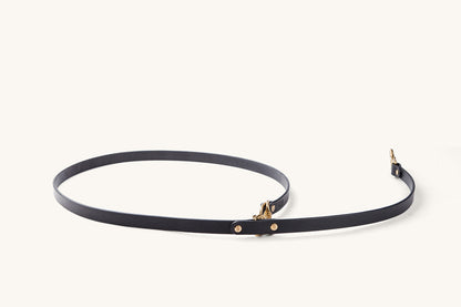 Black convertible canine lead with gold-toned hardware, loosely coiled on a white background.