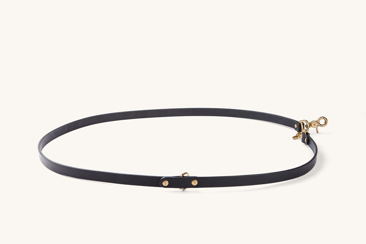 Black convertible canine lead, lying flat in an oval shape, with gold hardware and a swivel snap hook.