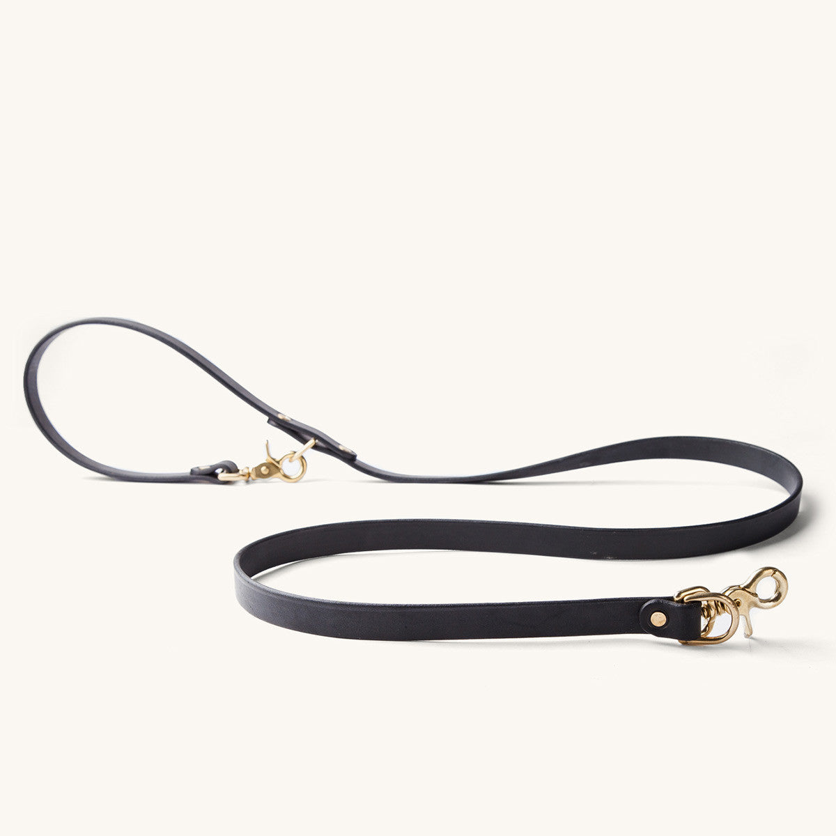 Black convertible canine lead with brass-tone clasps, arranged on a light background.