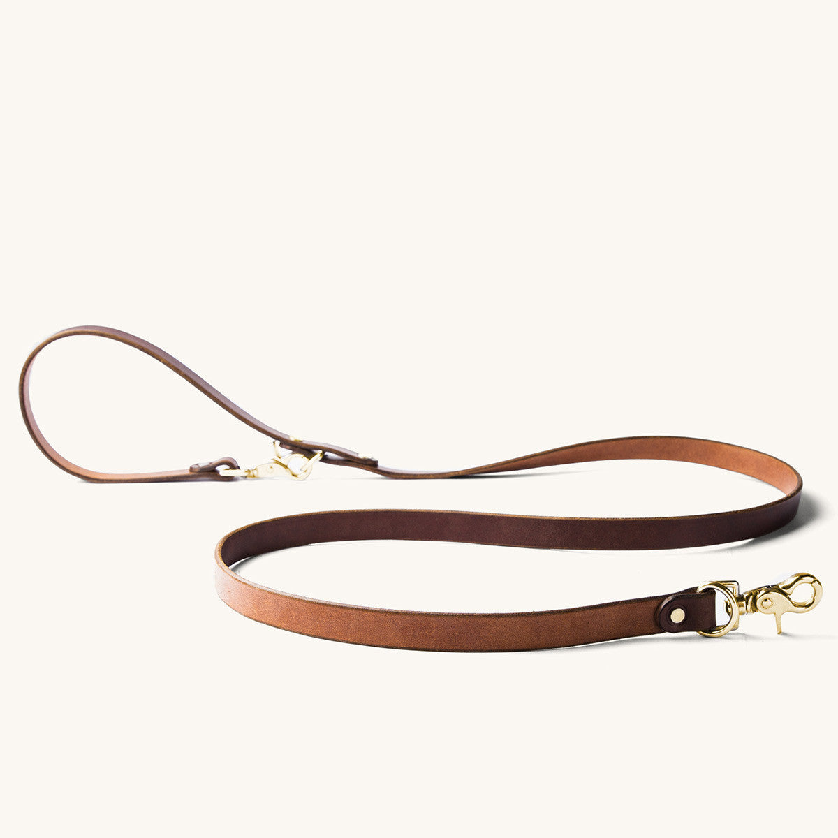 Cognac leather convertible canine lead with gold brass hardware, laid flat.