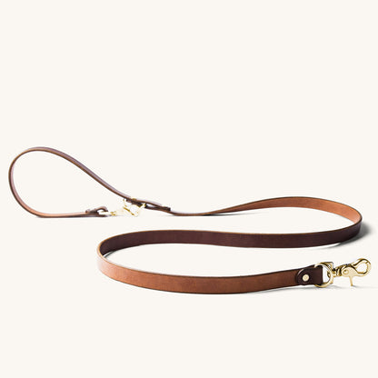 Cognac leather convertible canine lead with gold brass hardware, laid flat.