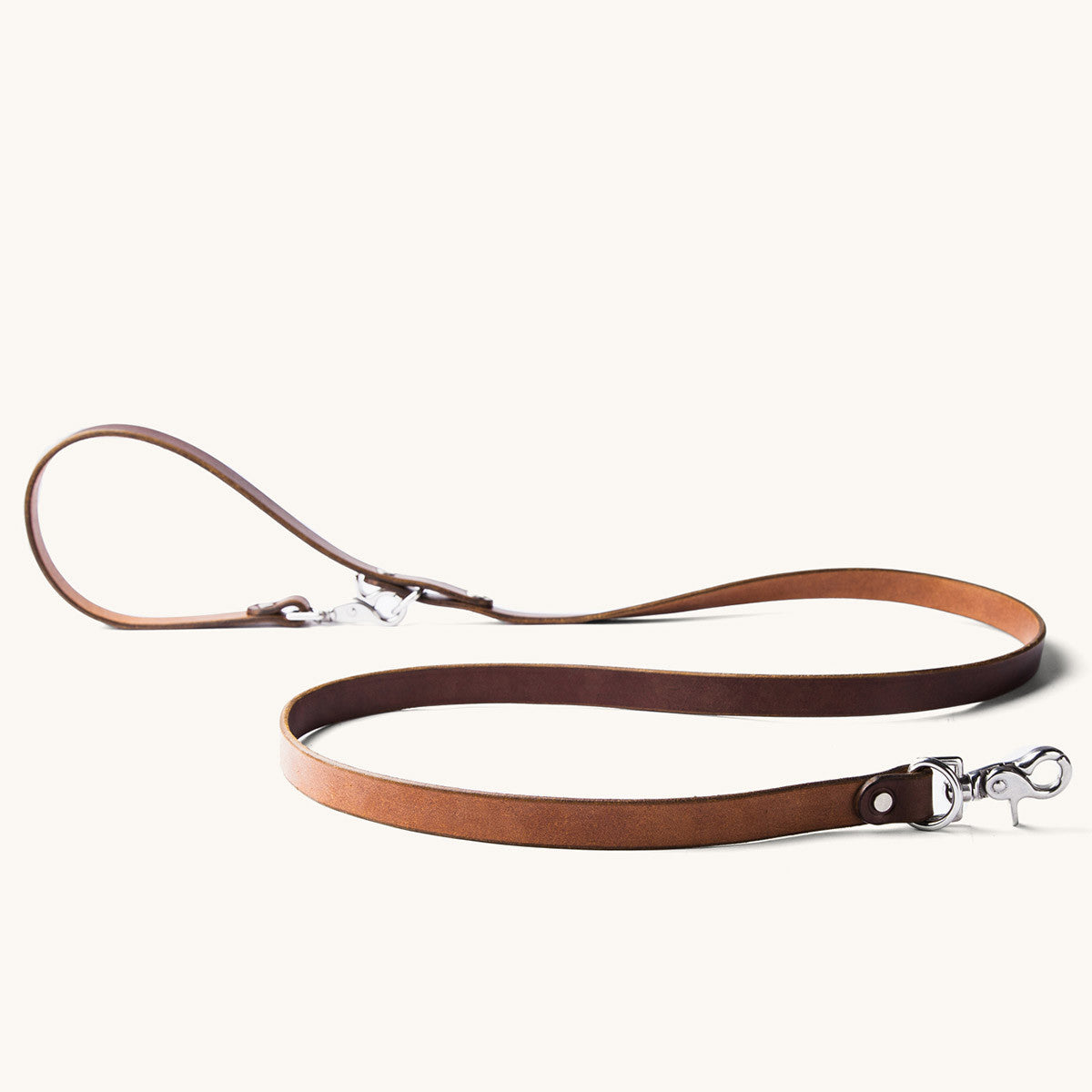 Cognac leather convertible canine lead with silver-toned hardware, laid on a light background.