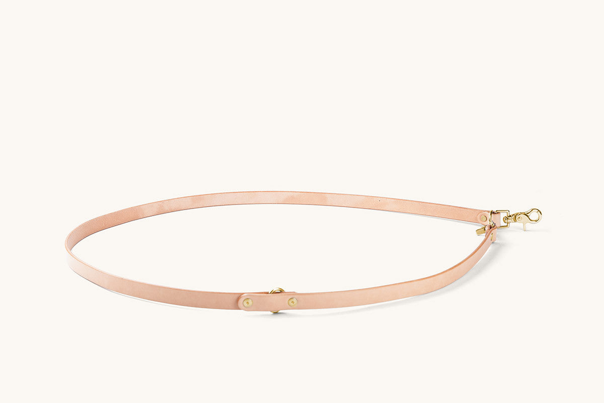 Natural leather convertible canine lead with gold-toned hardware, coiled on a light background.
