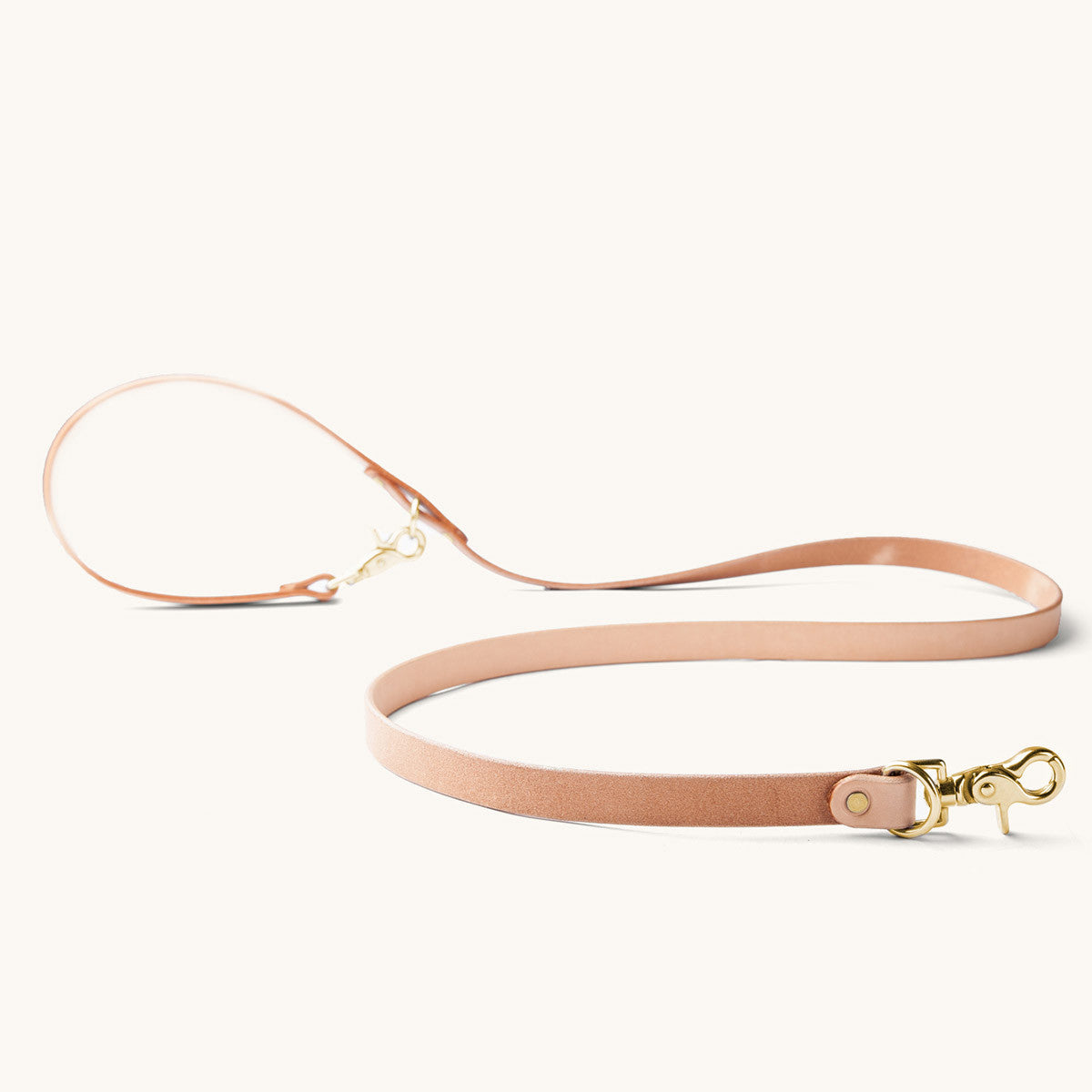 Natural leather convertible canine lead with gold metal snap hooks and rings, lying flat.