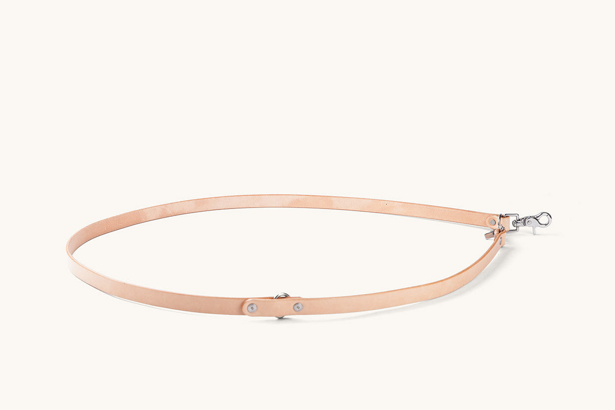 Natural leather convertible canine lead with a silver-toned snap hook and rivets, coiled in an oval shape.