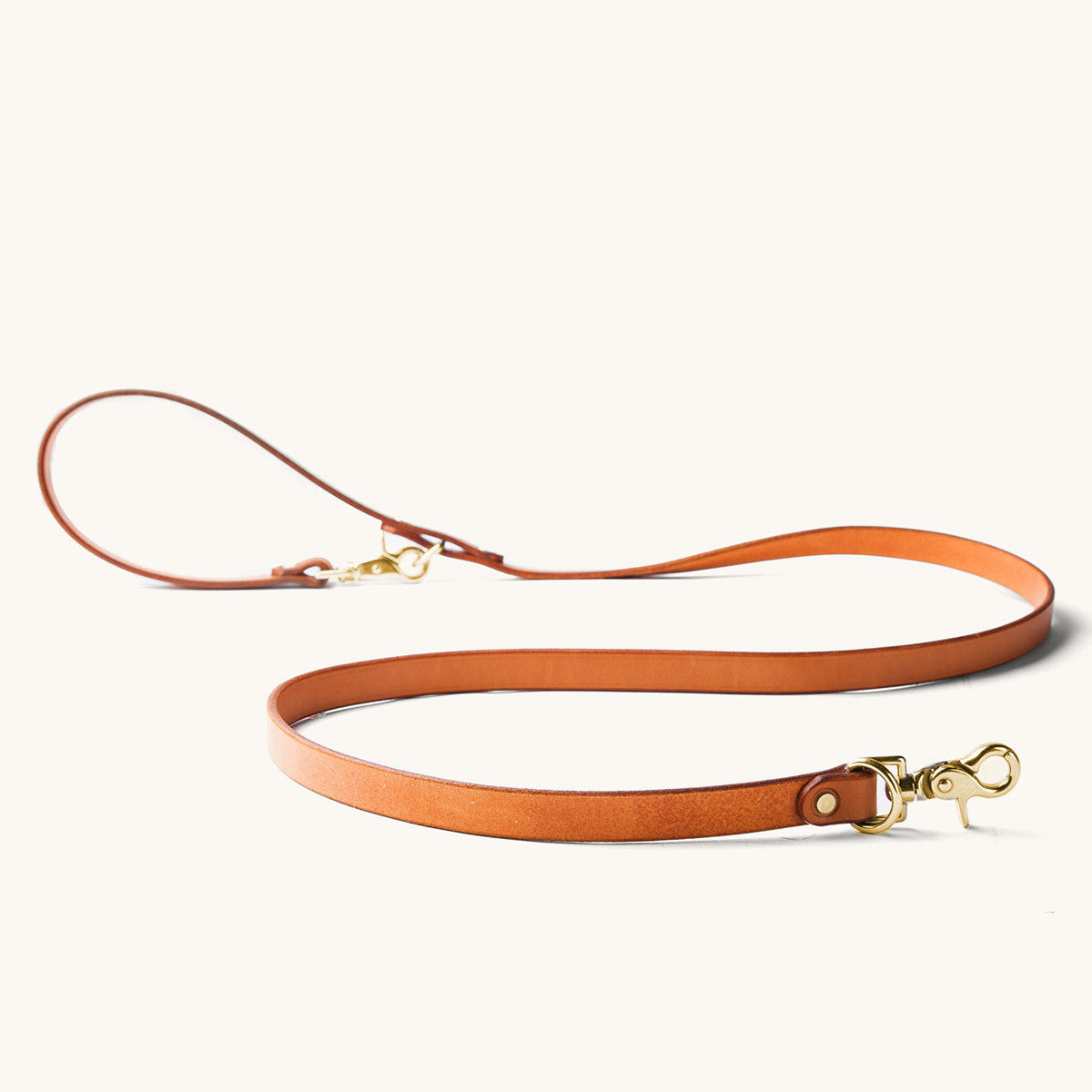 Convertible canine lead in saddle tan leather with brass hardware, laid in an S-shape.