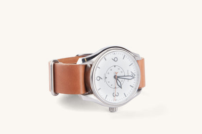 Cordovan leather NATO watch strap in natural tan, shown on a silver-toned watch with white dial and black numerals, side view.