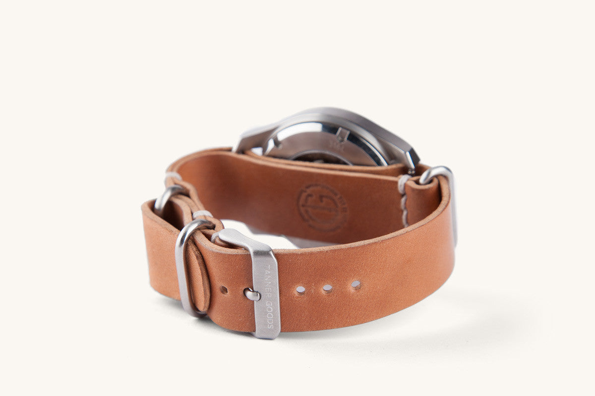 Cordovan leather Nato watch strap in natural tan by Tanner Goods, featuring silver hardware and embossed logo, side view on white background