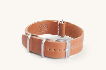 Cordovan leather NATO watch strap in natural tan with silver buckle and white stitching, side view, embossed logo on inner lining