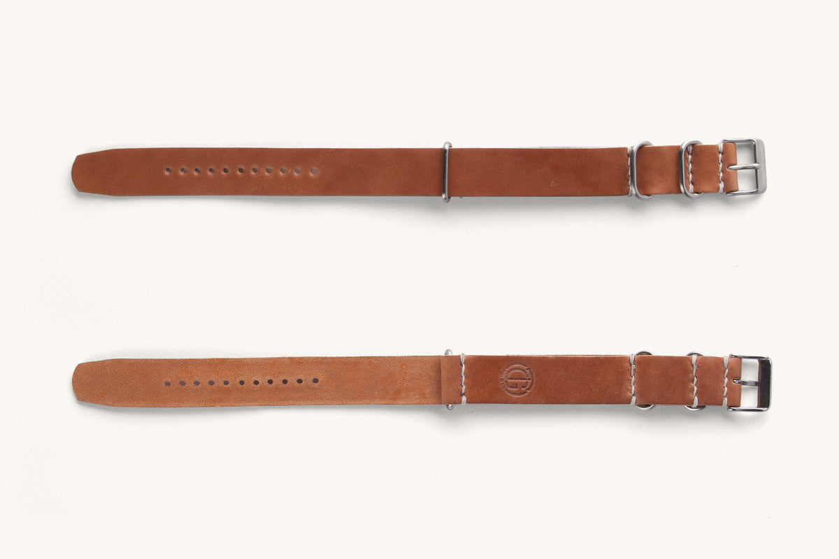 Cordovan leather NATO watch strap in natural brown, featuring silver-tone hardware and white stitching, shown flat with embossed logo on one side