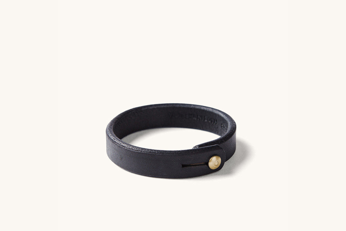 A black leather wristband with brass rivet closure.