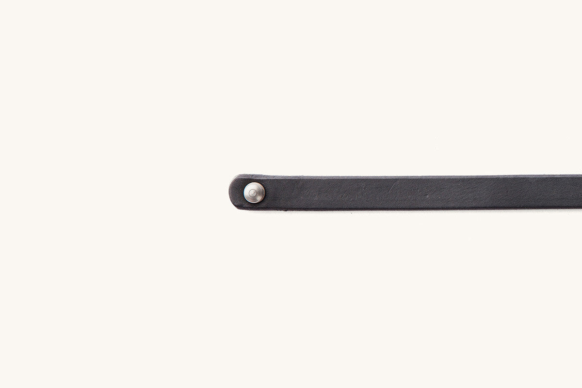 Flat black single wrap wristband, textured, with a round silver-colored rivet at one end.