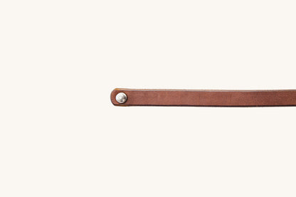 Cognac leather single wrap wristband with a silver metal stud, laid flat.