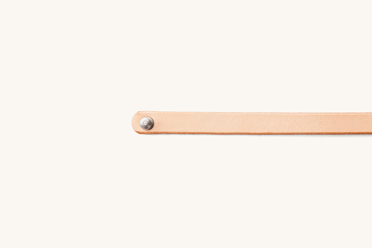 Natural single wrap wristband of light tan leather with a silver rivet on a rounded end.