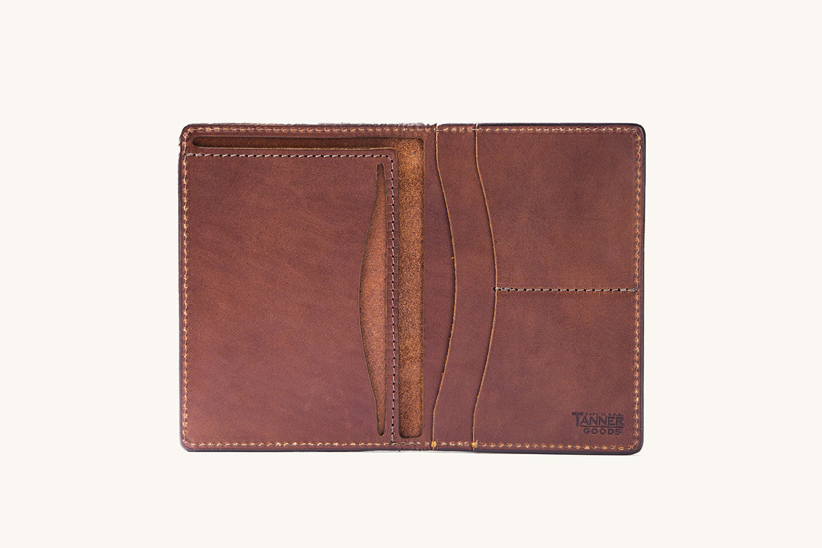 Cognac brown leather travel wallet by Tanner Goods, open to show multiple card slots and pockets with visible stitching.