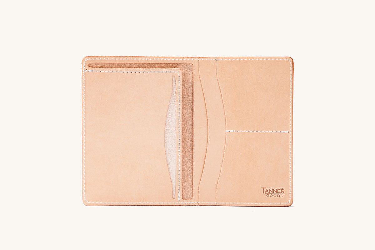 Natural leather travel wallet by Tanner Goods, open to reveal multiple card slots and pockets with white stitching.