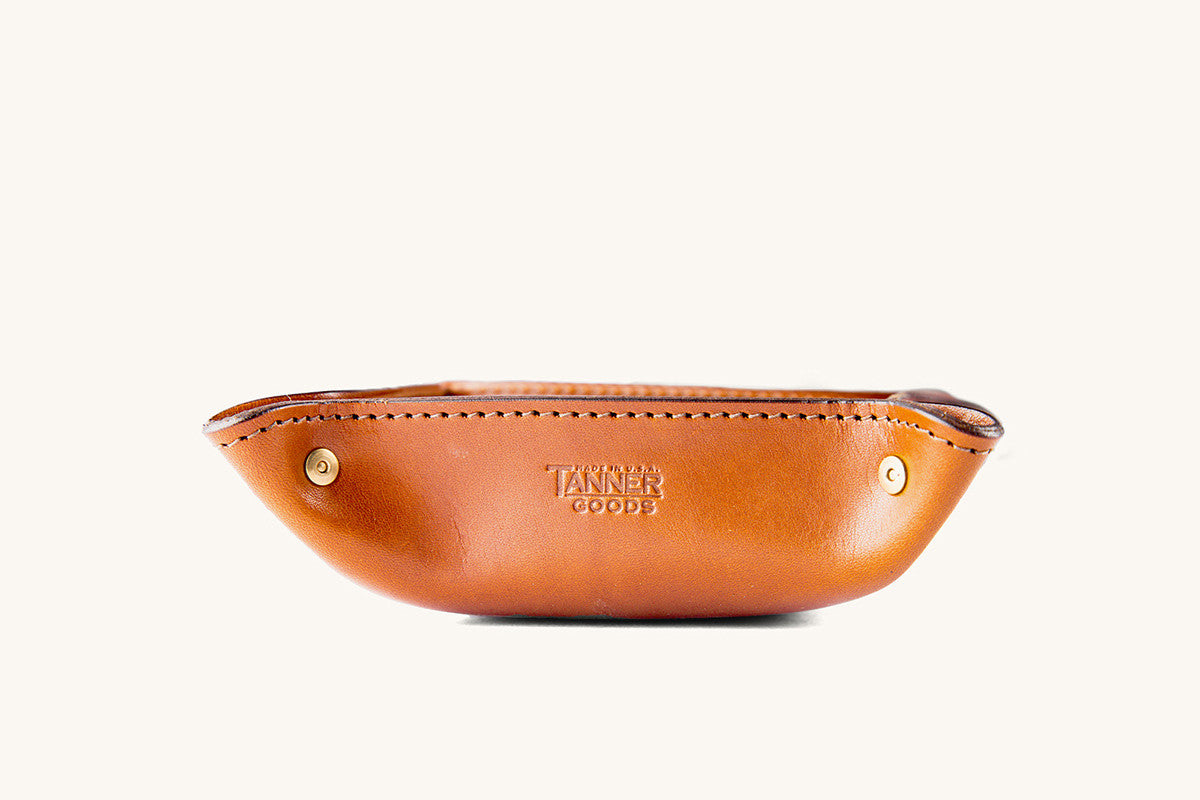 Saddle tan leather valet tray by Tanner Goods with gold snaps and an embossed logo, viewed from the side.